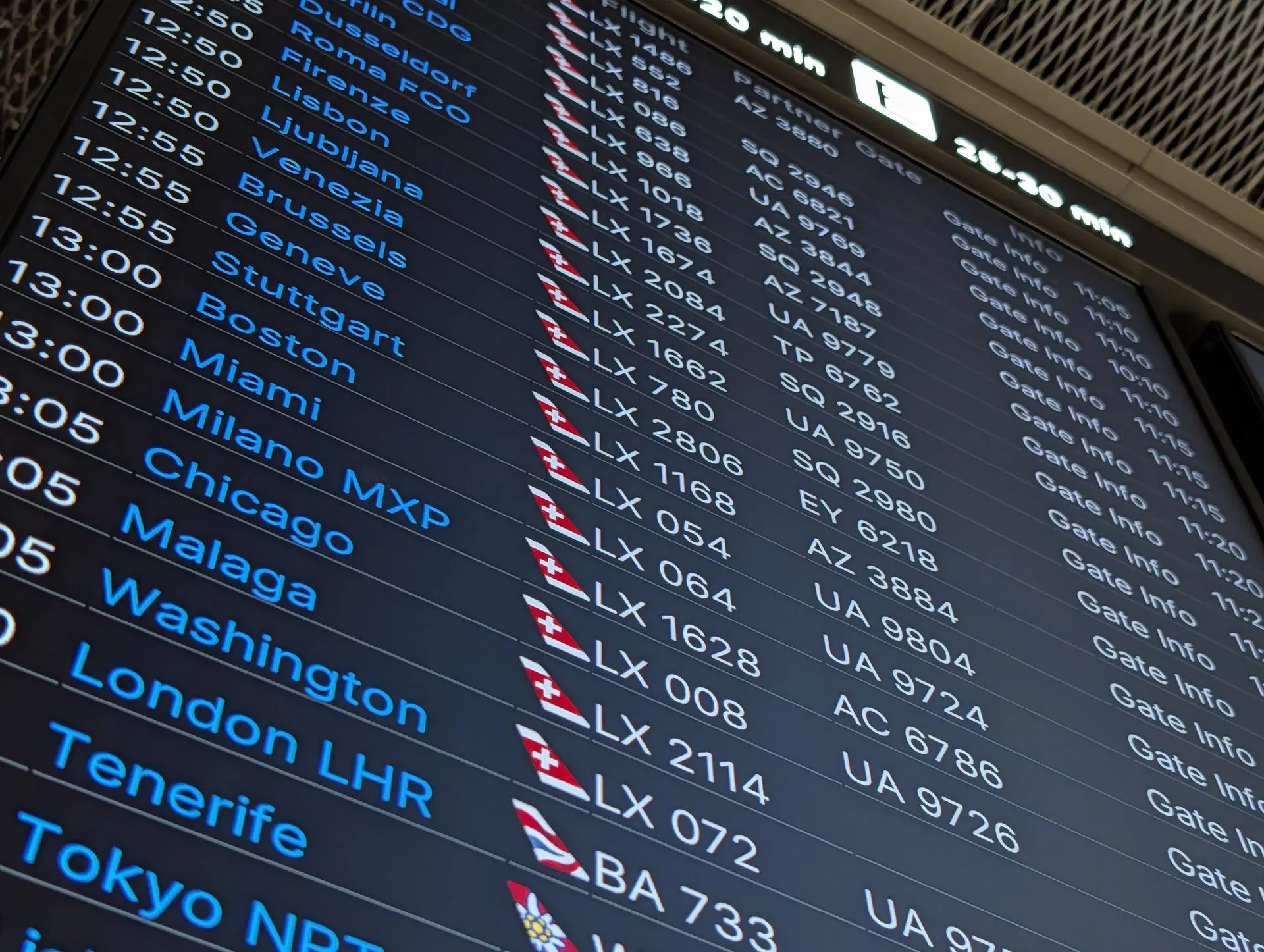 A departures board at Zurich Airport listing flights to Malaga, Washington, London and Tokyo with their departure times and flight numbers