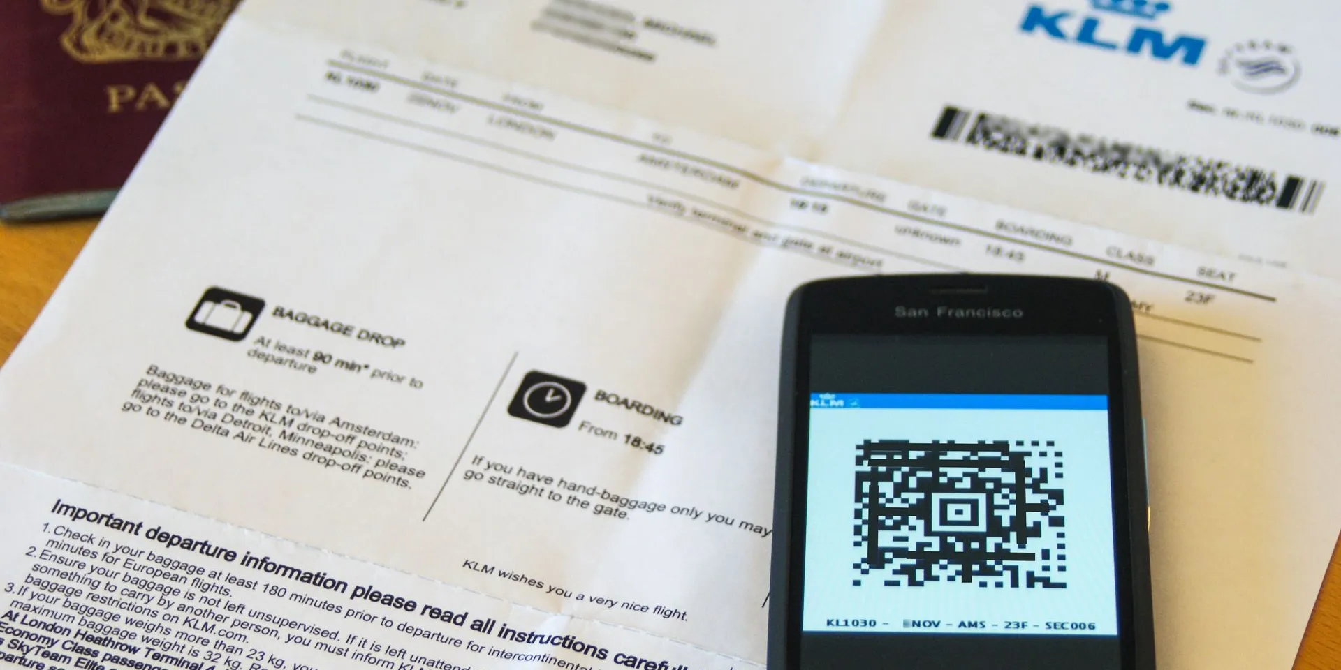 A printed boarding pass beside a phone showing the same boarding pass as a QR code, with a passport in the corner