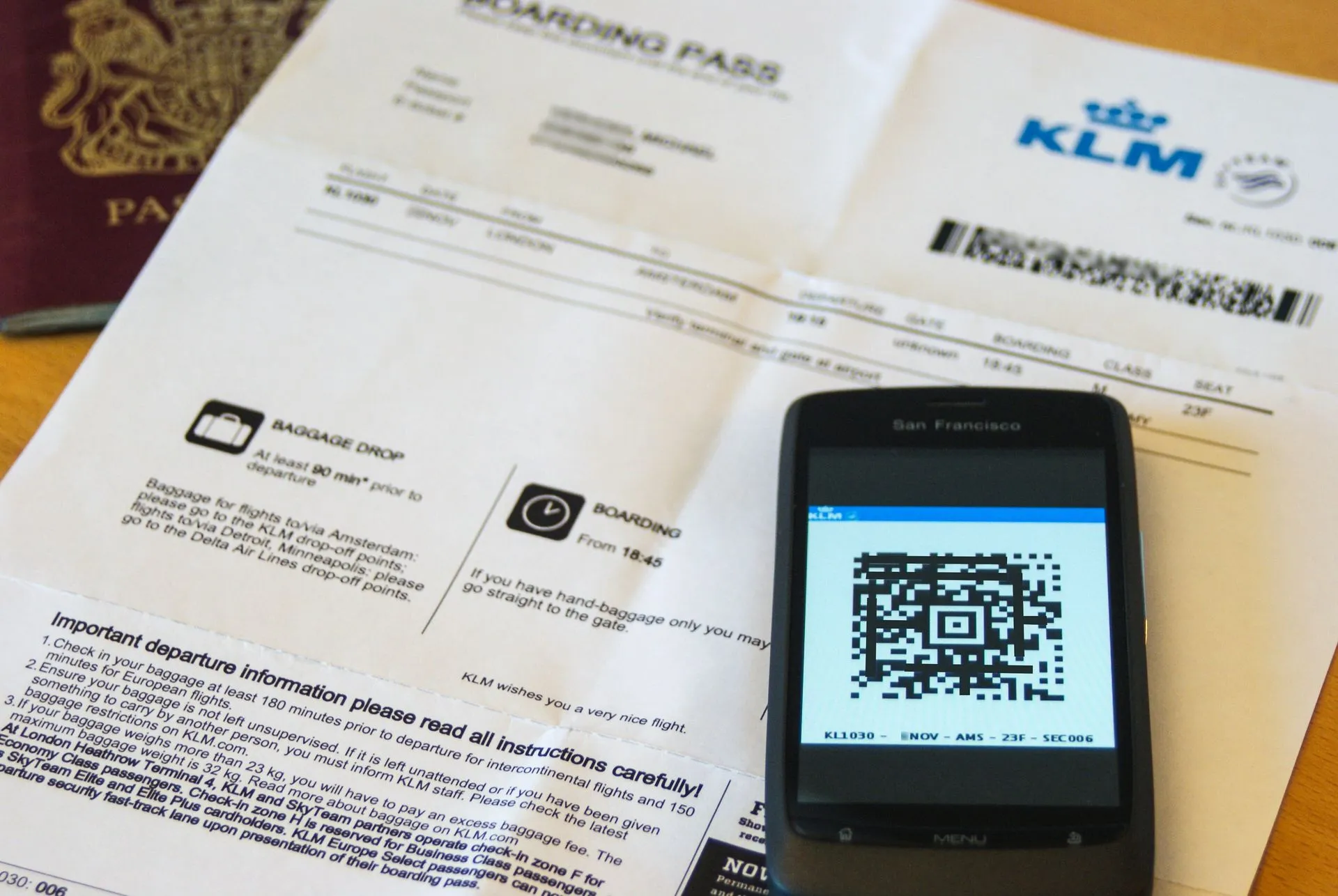 Una tarjeta de embarque impresa junto a un móvil que muestra la misma tarjeta como código QR, con un pasaporte en la esquina