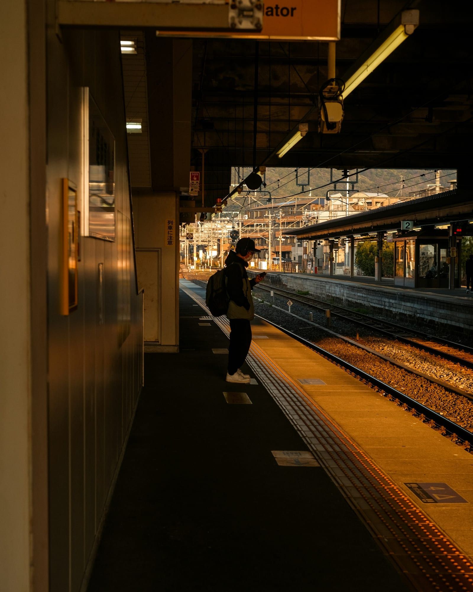 A traveler checks their phone on a station platform in Kyoto at sunset